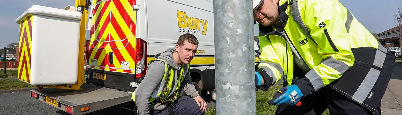 Two people looking at a street lighting column next to a cherry-picker vehicle