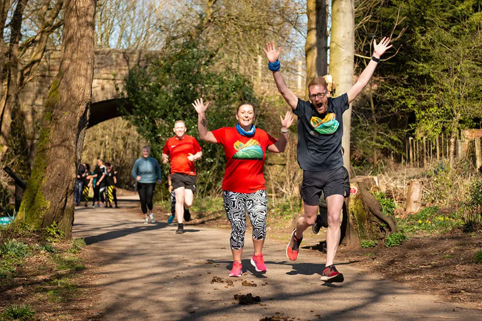 A group runners on a countryside lane,  smiling and waving with trees in the background
