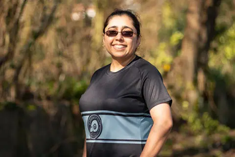 Smiling person wearing sunglasses and a black t-shirt with trees in the background