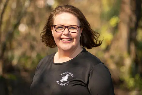 Smiling person wearing glasses and a black t-shirt with trees in the background