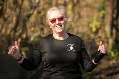 Smiling person wearing sunglasses, giving the thumb-up sign with trees in the background