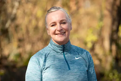 Smiling person wearing a running top with trees in the background