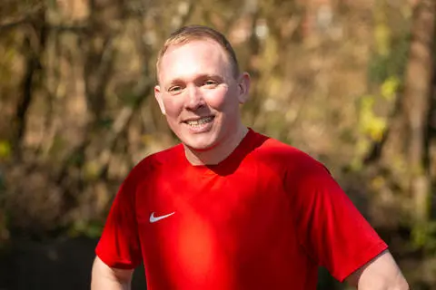 Smiling person wearing a red t-shirt with trees in the background