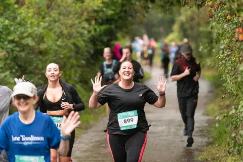 A group of people running on a countryside lane, smiling and waving