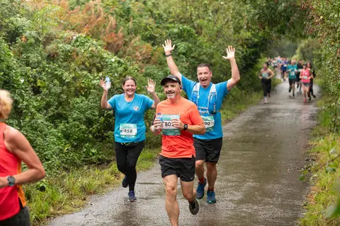 A group of people running on a countryside lane, smiling and waving
