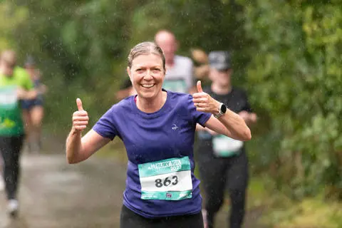 A person running on a countryside lane giving the thumbs up sign
