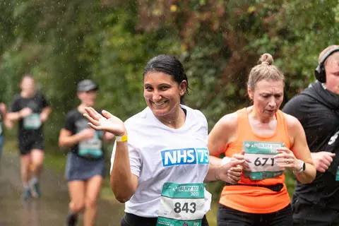 A person wearing an NHS 75 t-shirt running alongside other people on a countryside lane