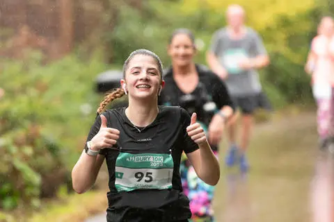 A person running on a countryside lane, smiling and giving the thumbs up sign
