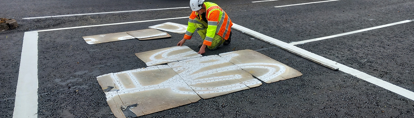 A person wearing high-visibility clothes painting a graphic of a bicycle on the road surface