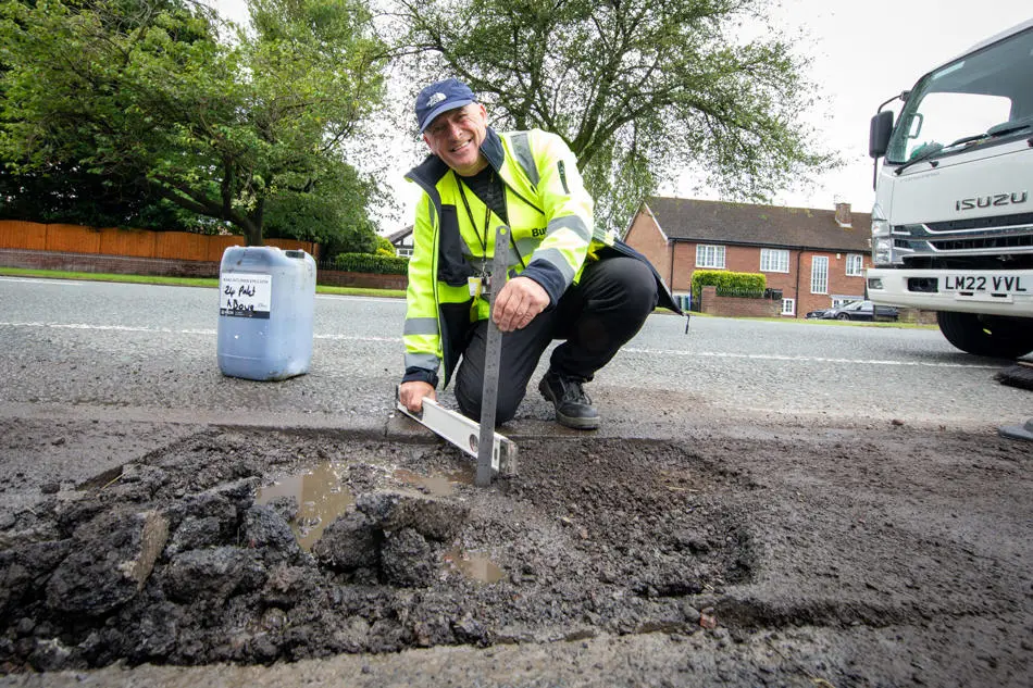 A person holding a measure and a spirit level over a defect in the road