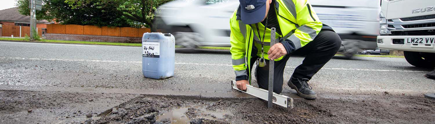 A person holding a ruler and a spirit level over a pothole in the road