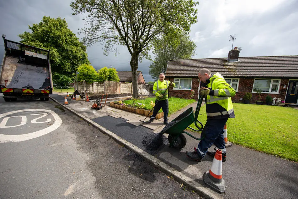 A person pouring tarmac from a wheelbarrow onto a footway