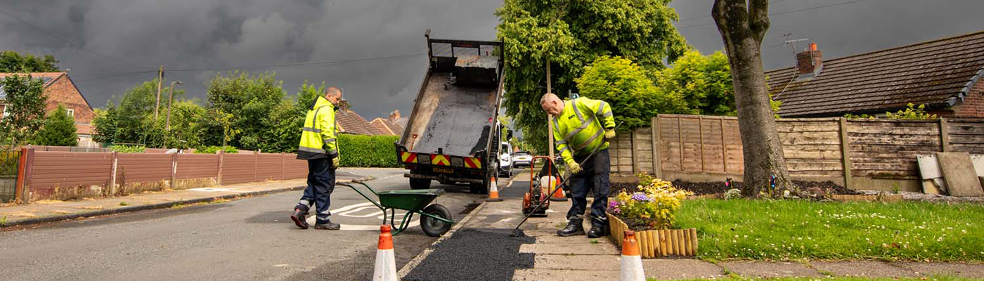 A person wearing high-visibility clothing using a rake to put tarmac onto a pavement