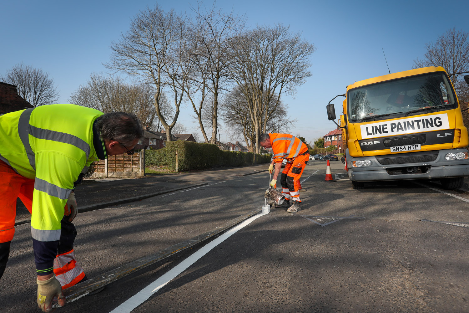 Two people painting a white line on a road surface