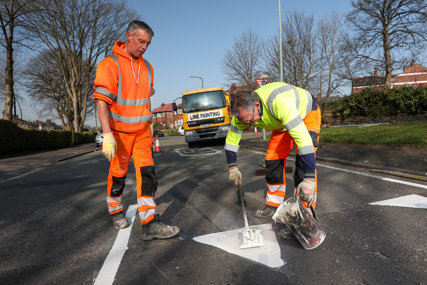 Two people painting a white triangle on a road surface