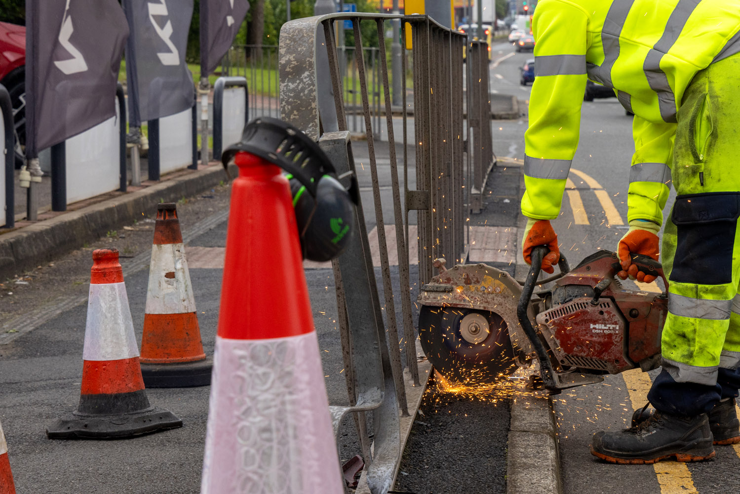 A person wearing personal protective closing using cutting equipment on a railing on the roadside