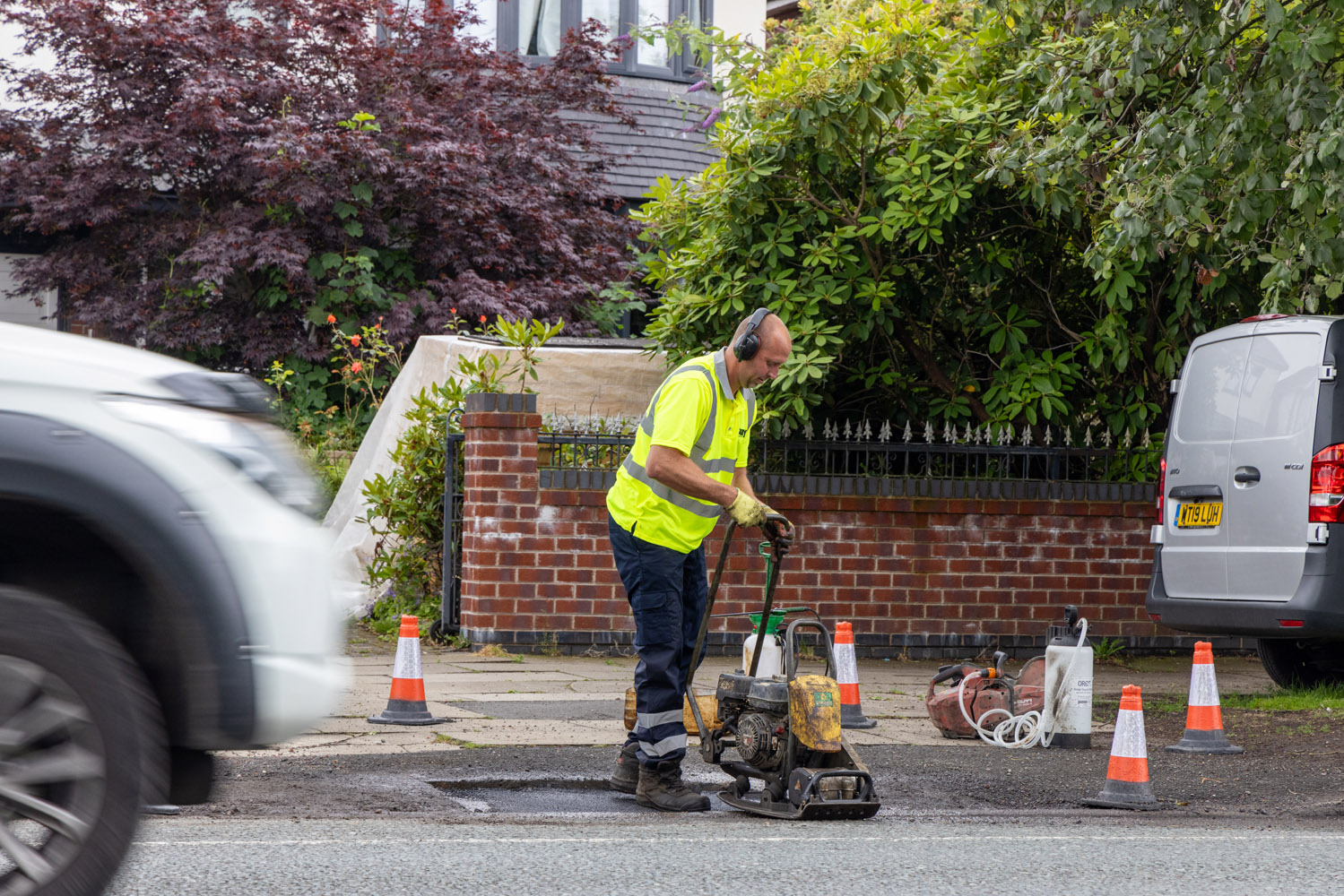 A person using a handheld compactor to press tarmac into a pothole on a road surface