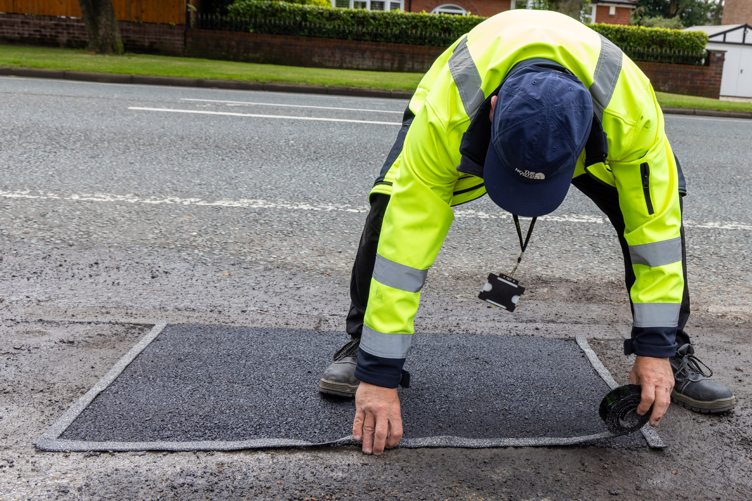 A person using their hands to seal a pothole repair on a road surface
