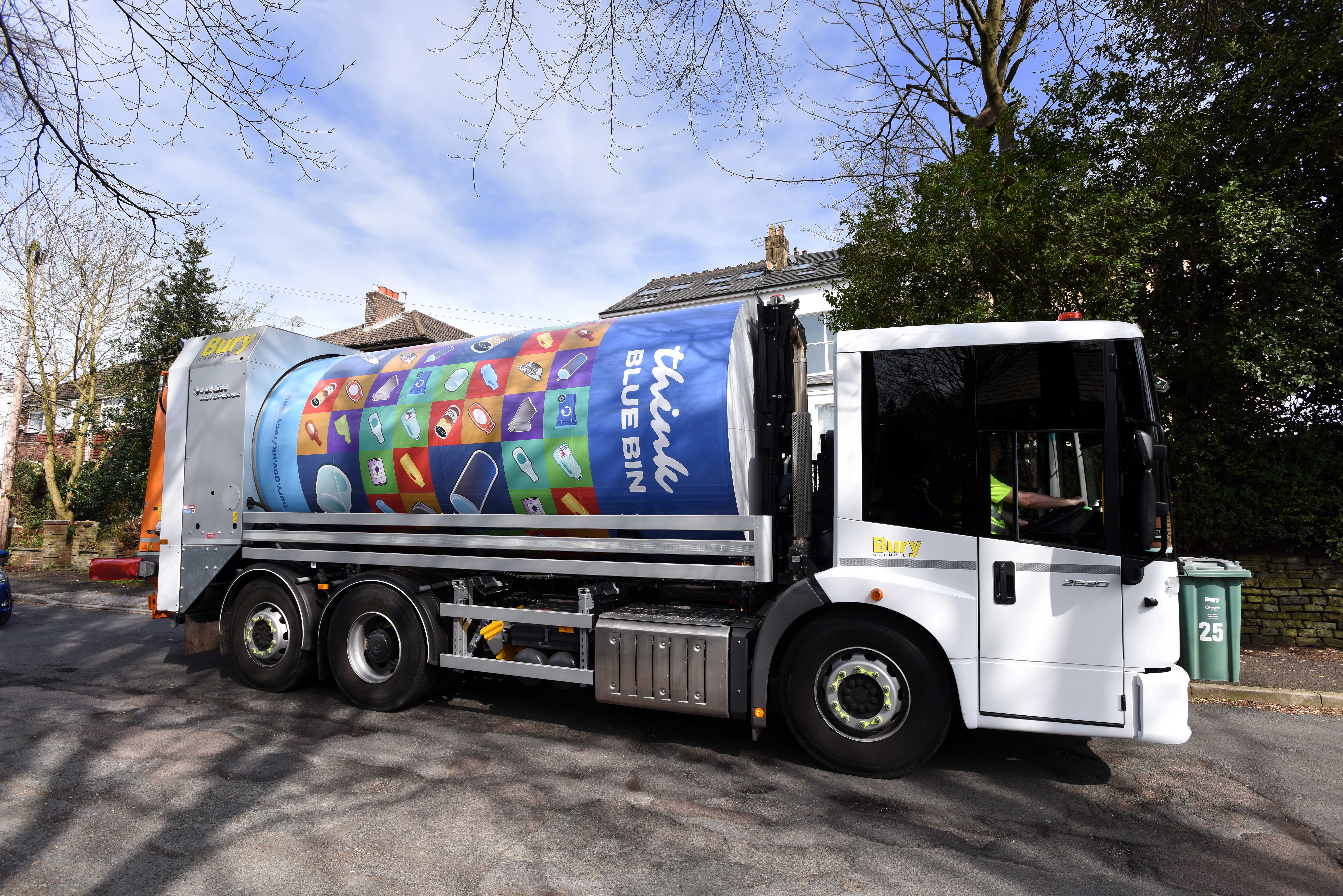 A side on view of a bin collection truck travelling along a residential street