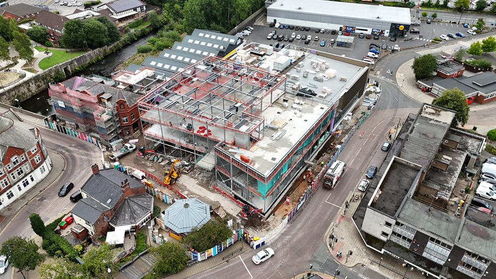 A large building on a construction site surrounded by a road and buildings