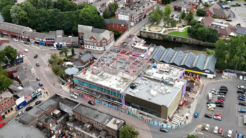 A large building on a construction site surrounded by a road, buildings and a small park