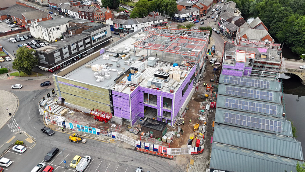 A large building on a construction site surrounded by a road and buildings