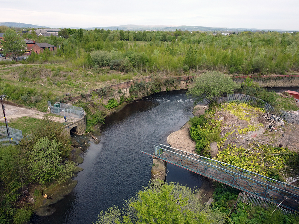 A broken bridge over a river surrounded by trees and greenspace