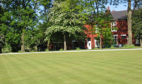 Bowling green by trees and houses.