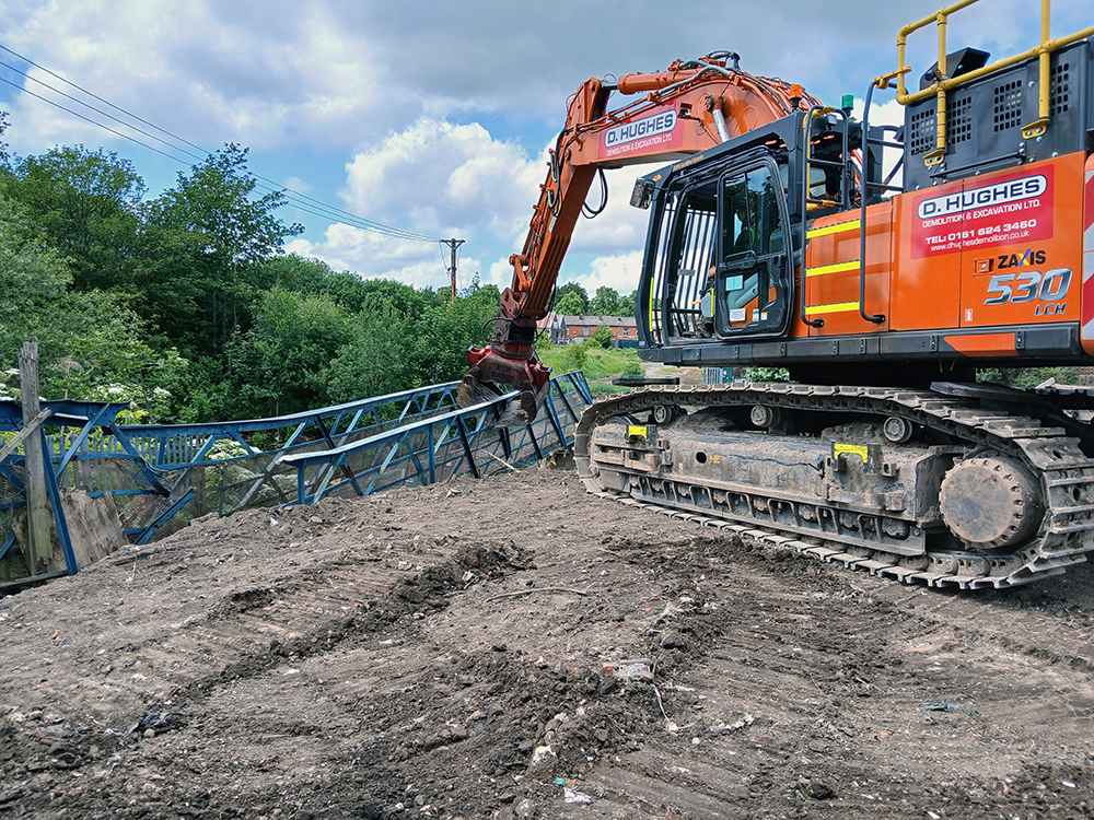 A heavy construction vehicle with a claw attachment tearing down a metal bridge