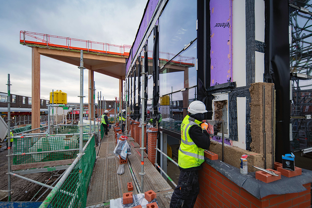 A person wearing high visibility safety clothing installing a large window on a large building that is under construction
