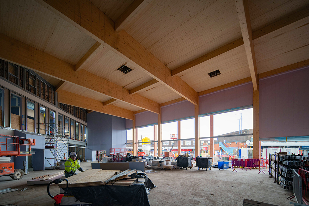 The inside of a large building that is during the construction stage. The building has a wooden ceiling and large windows along one side.