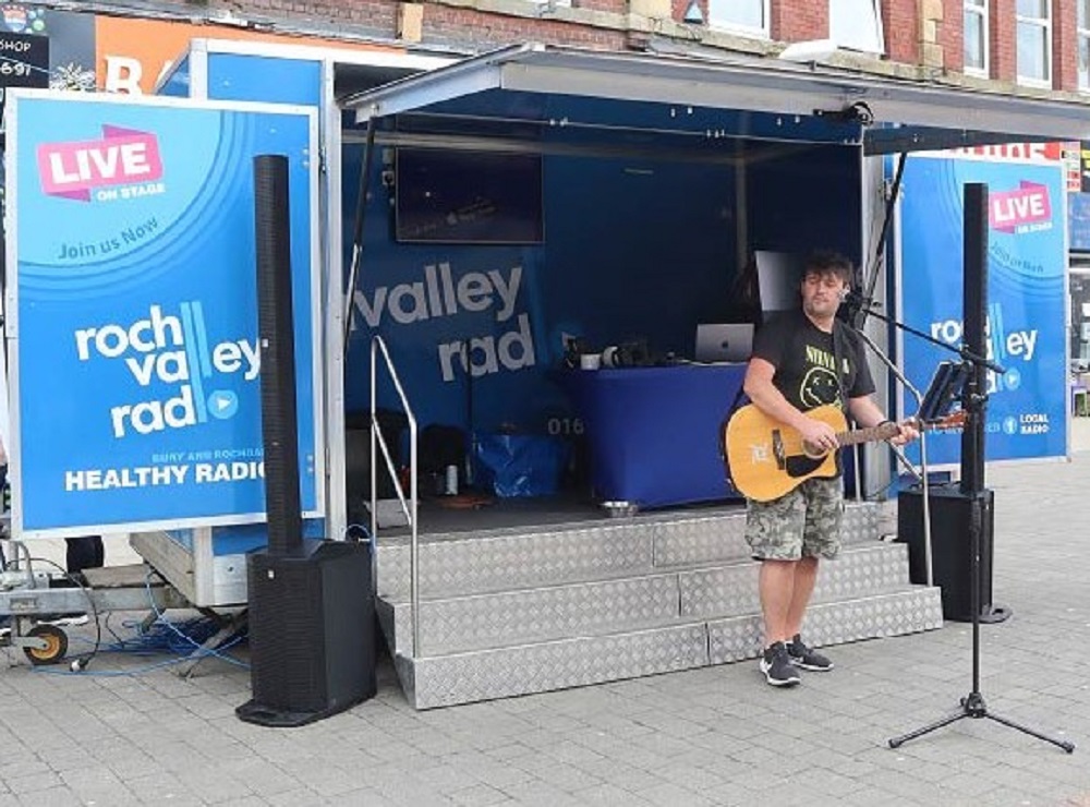 Person stood in front of a microphone playing a guitar.