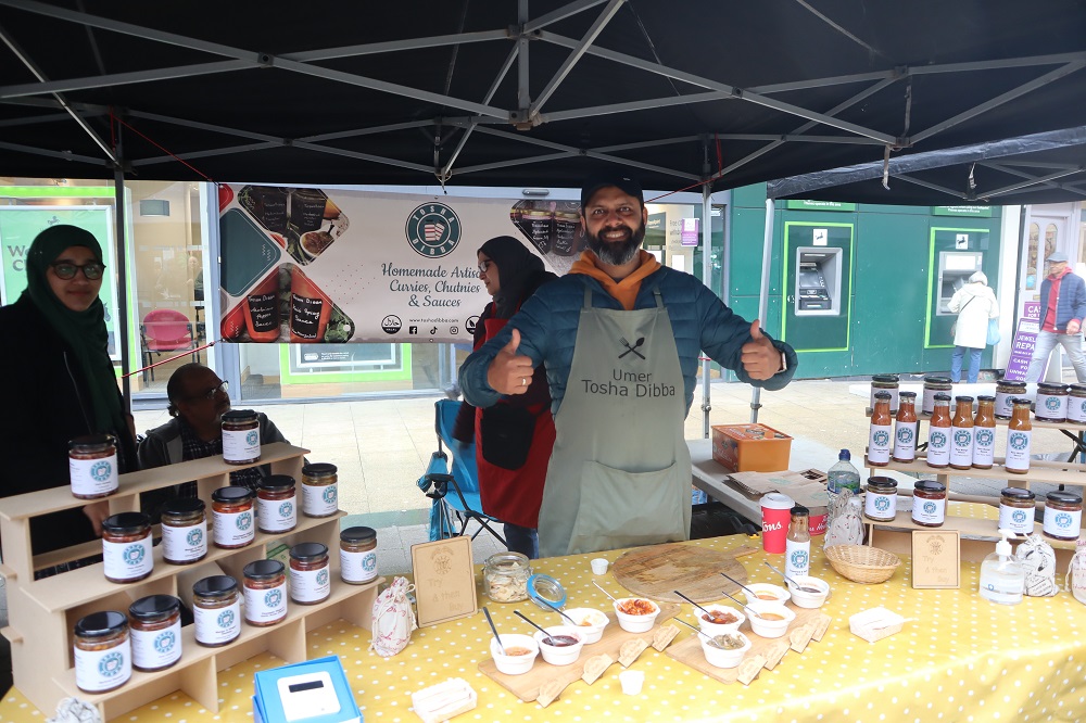 Person stood behind a table giving the thumbs up.
