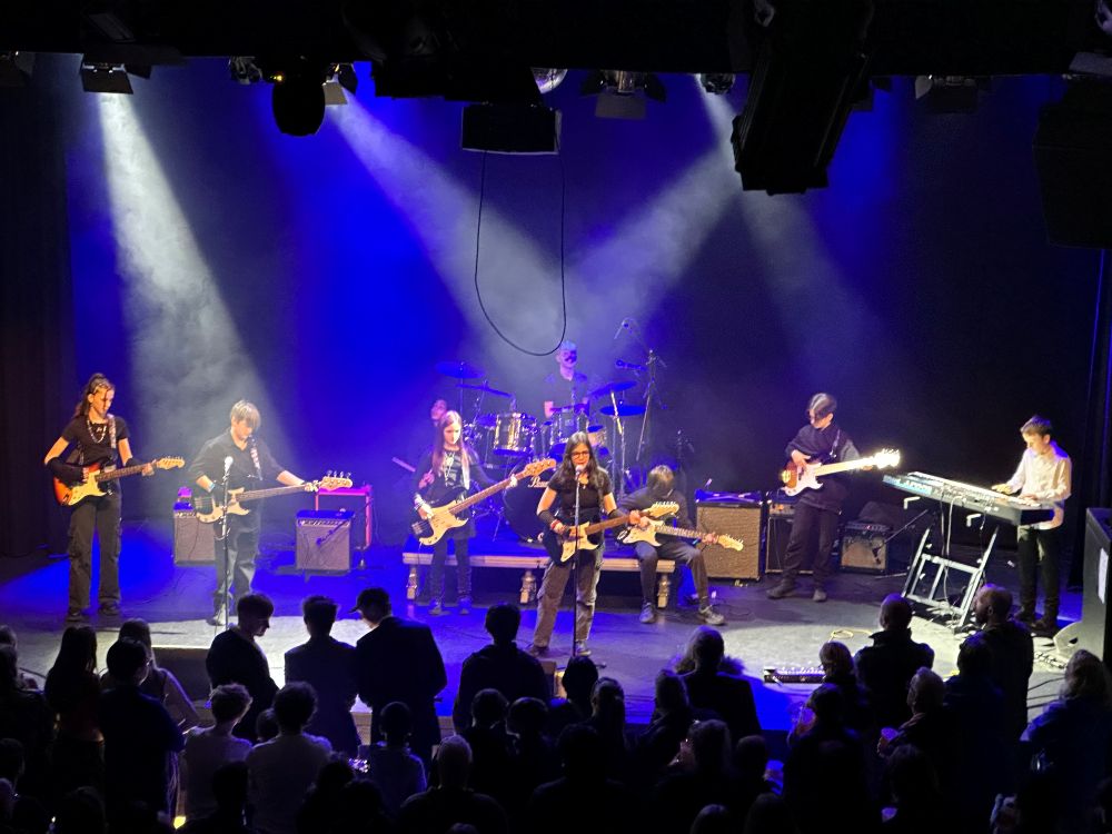 Young music students standing on a stage playing instruments.