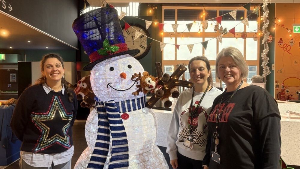 Three ladies stood next to a large snowman decoration.