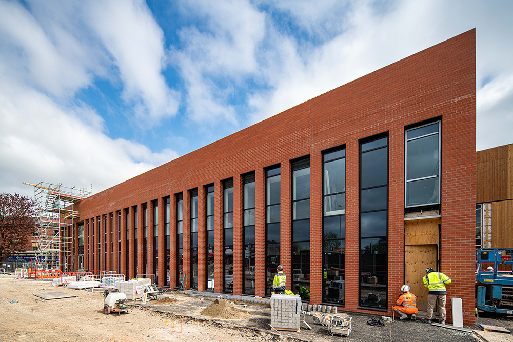 Construction workers on the site of large brick building with floor to ceiling windows