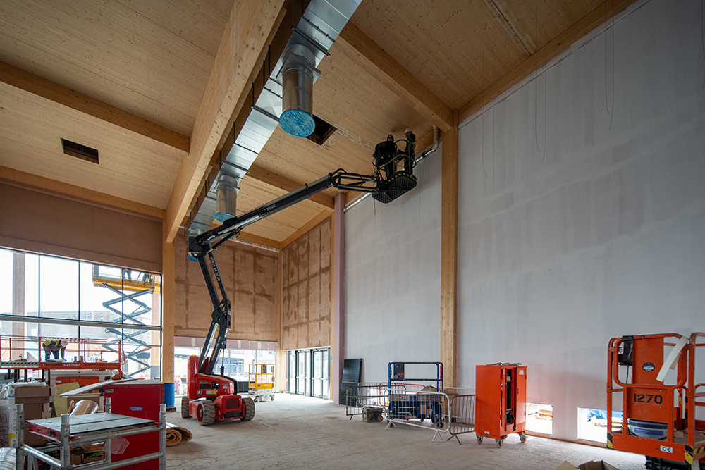 A construction worker in a cherry picker installing wood panels in to the inside of a large building