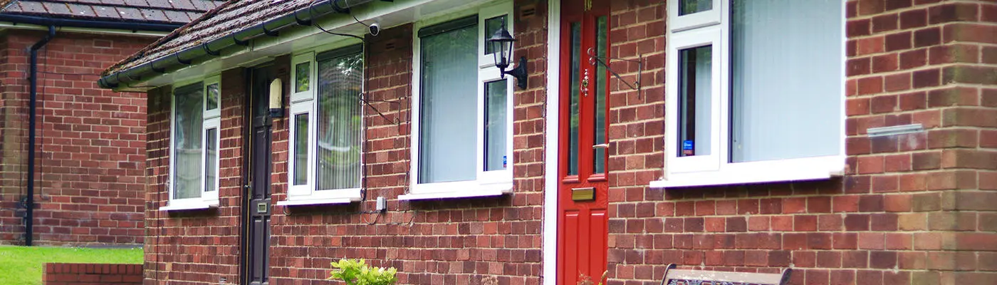 The front of two one-storey houses. Each house has one door and two windows.
