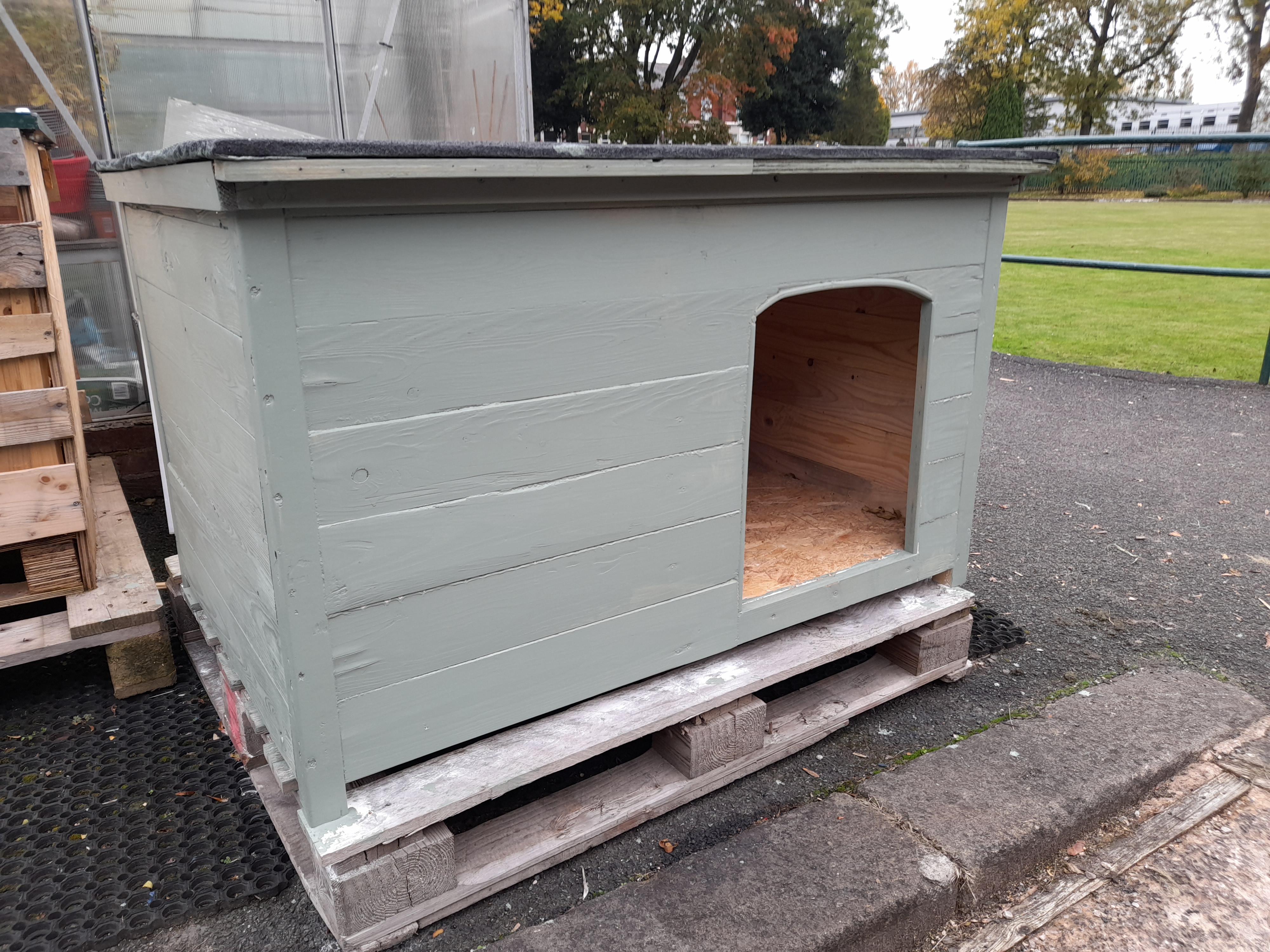 Wooden dog house painted in sage green.