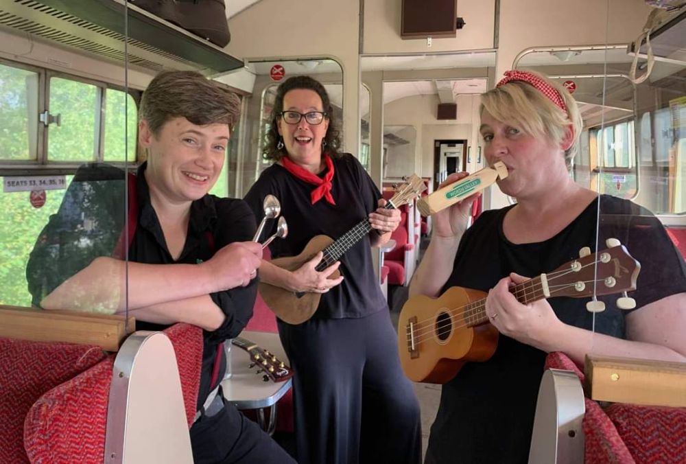 Three people playing musical instruments in a train carriage.