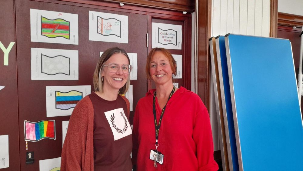 Two people standing in front of a wall that contains drawings by children.