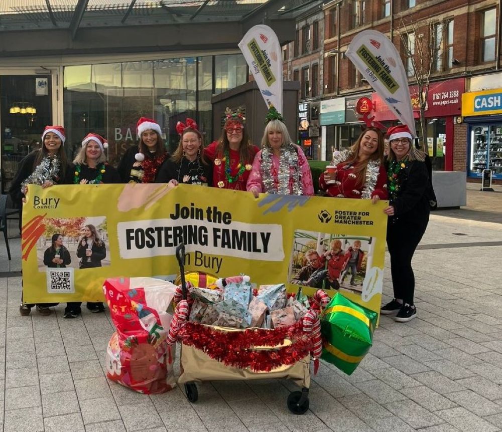 A group of people in fancy dress stood behind a banner that reads 'Join the Fostering Family in Bury'.