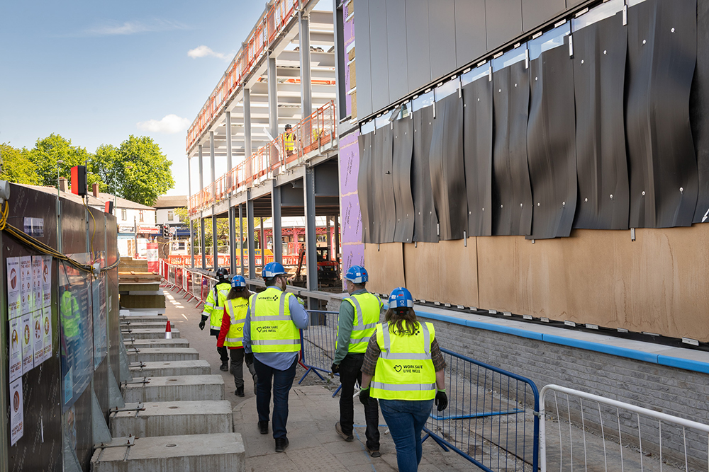 A group of people wearing protective clothing who are walking alongside a building on a construction site