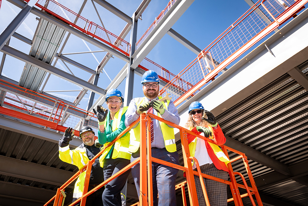 A group of people holding gold coloured bolts who are high up in a building on a construction site