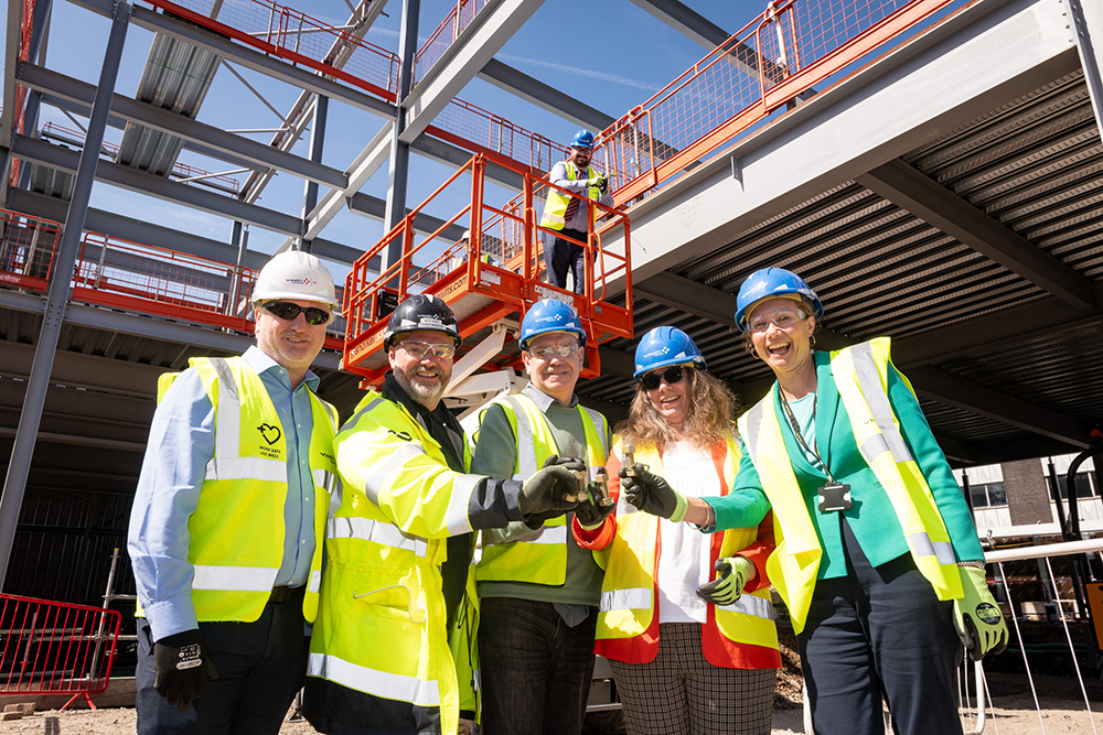 A group of people holding gold coloured bolts who are standing in a construction site