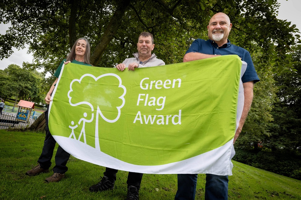 Three people holding a flag. The flag reads 'Green Flag Award'.