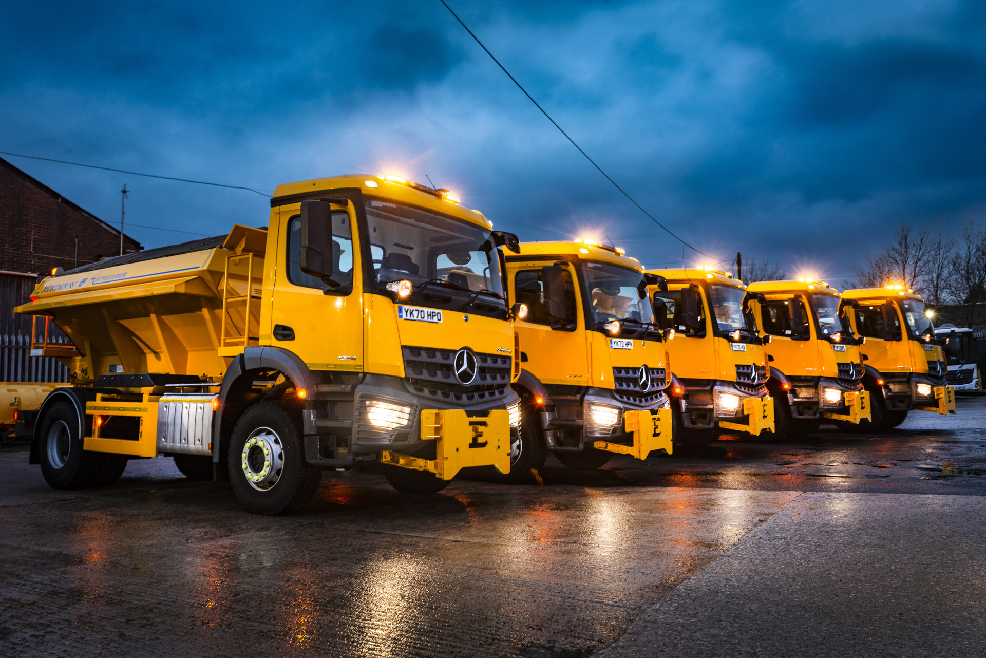 Five yellow gritting vehicles parked up in a service yard