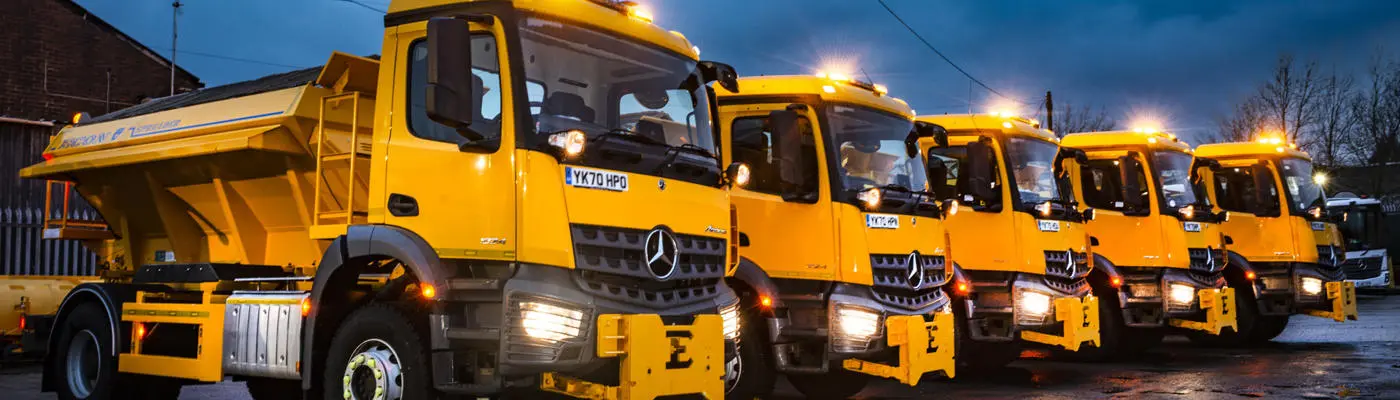 Five yellow gritting vehicles parked up in a service yard
