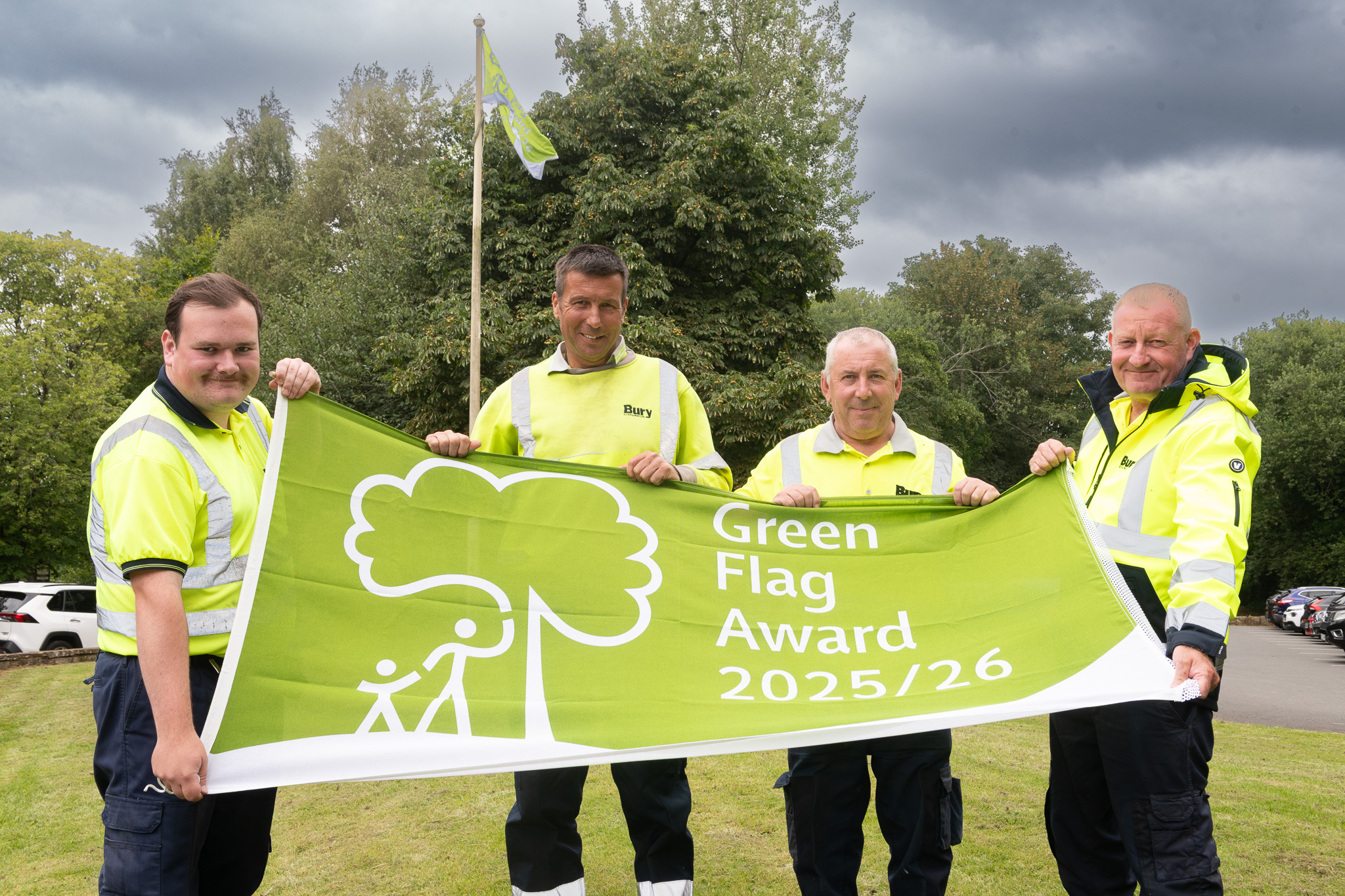 Four people standing on a grassed area holding a Green Flag award flag