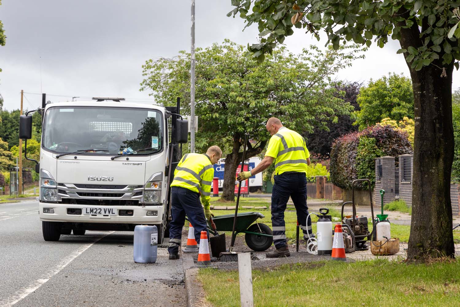 Two people in high visibility clothing digging on a roadside